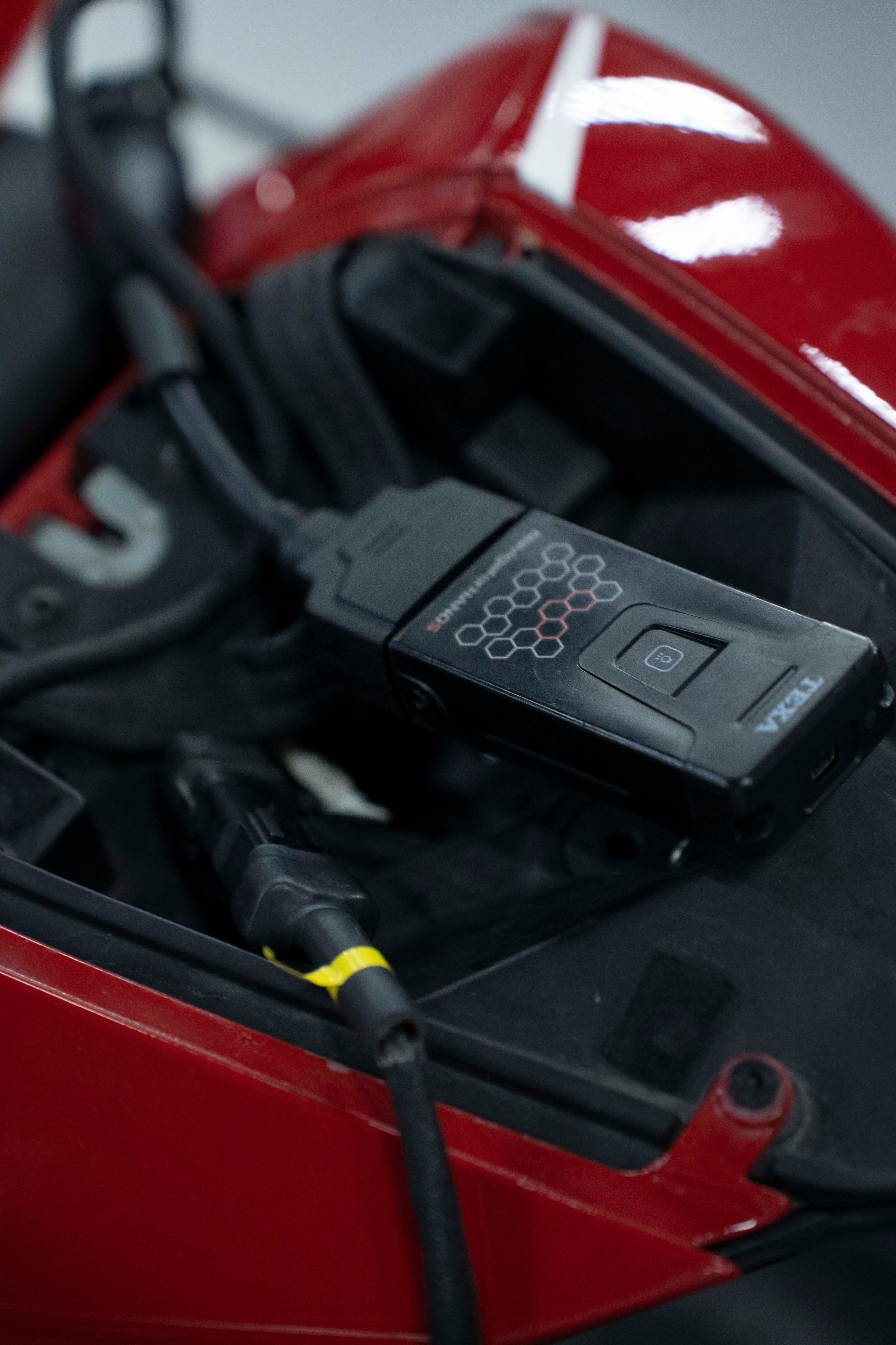 Black TEXA Navigator diagnostic tool plugged into the electronic port of a red motorcycle.