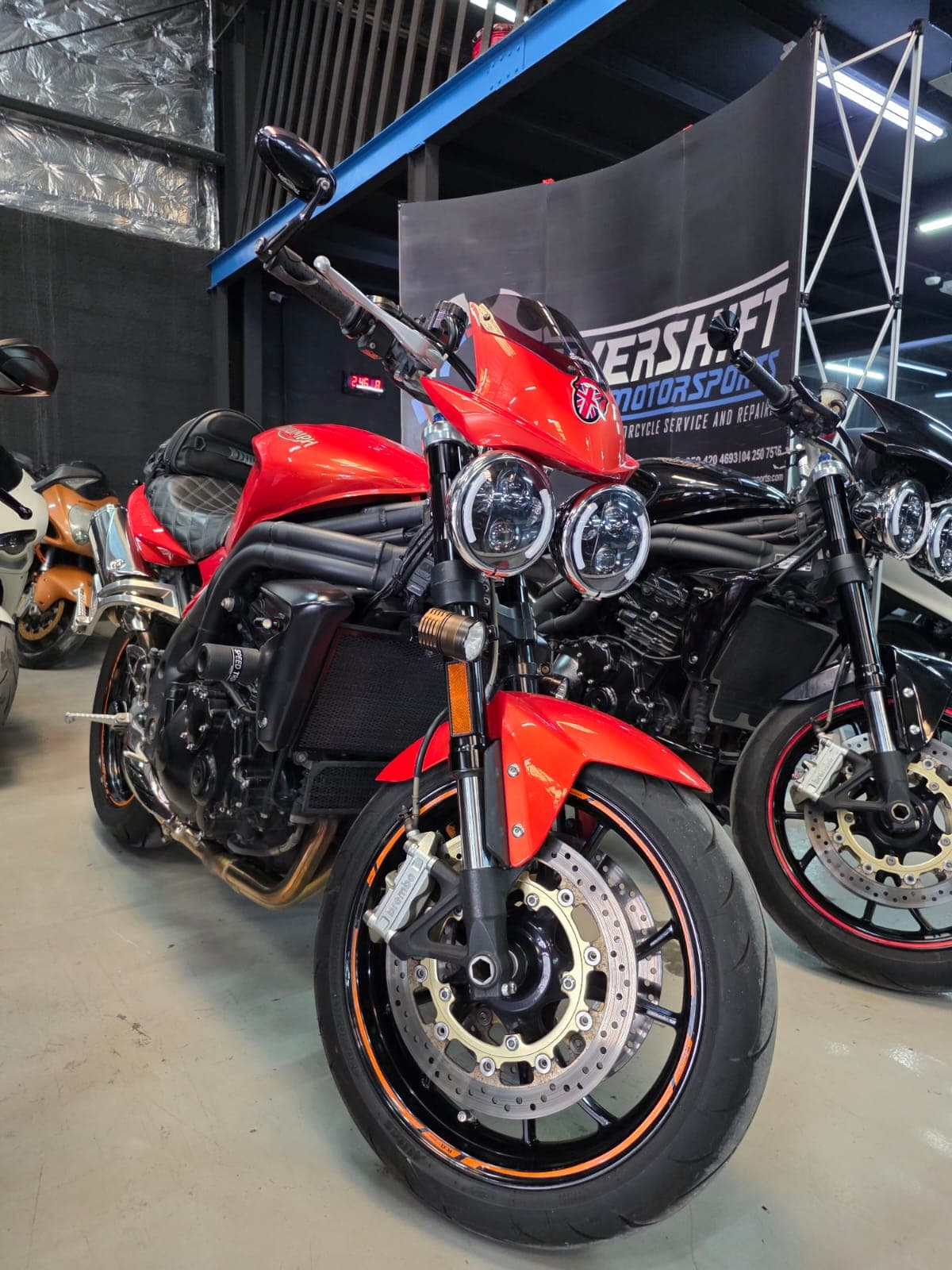 Red Triumph Speed Triple motorcycle with dual round headlights parked in a motorcycle service shop.