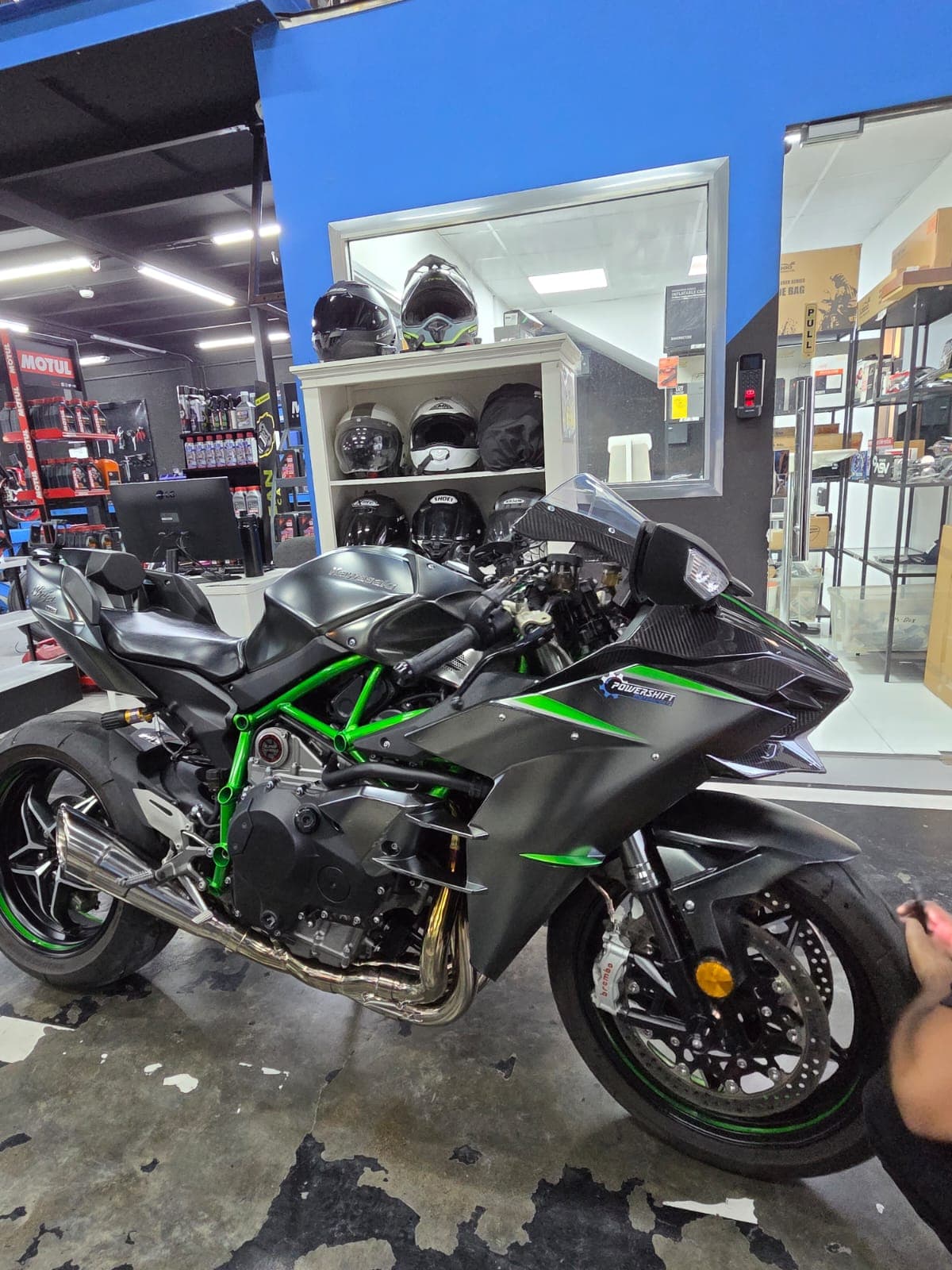 Matte grey Kawasaki Ninja H2 motorcycle featuring a vibrant green frame inside a showroom.